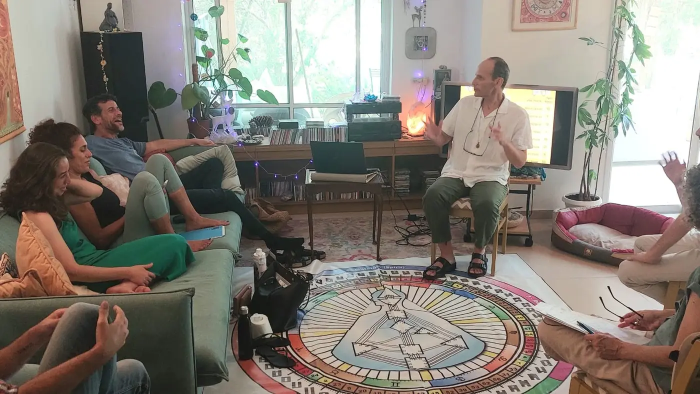 קבוצת לימוד יושבת בסלון סביב מנדלת הרייב, ודביר יצחקי מלמד